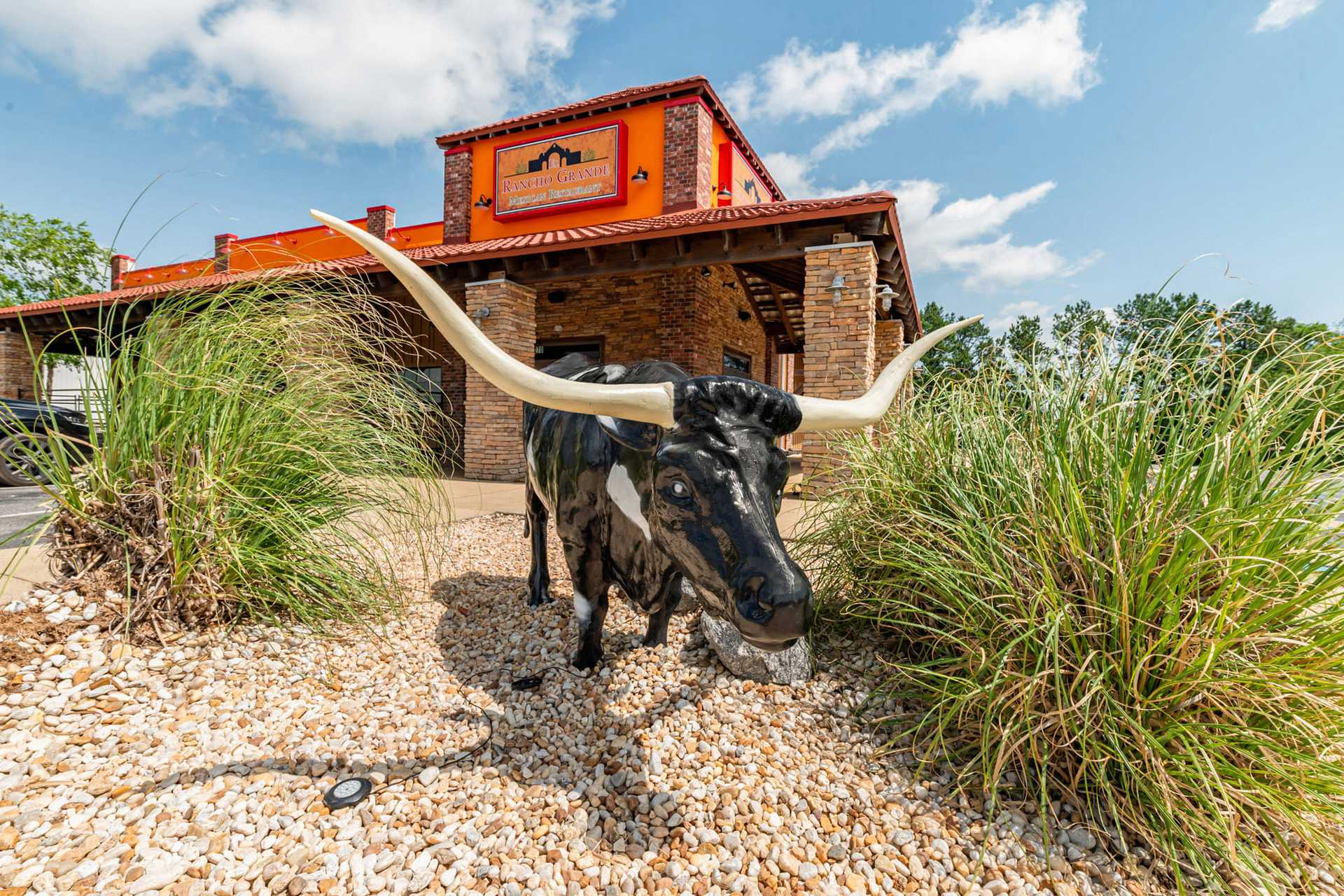Longhorn statue outside rustic restaurant with stone exterior and orange sign.