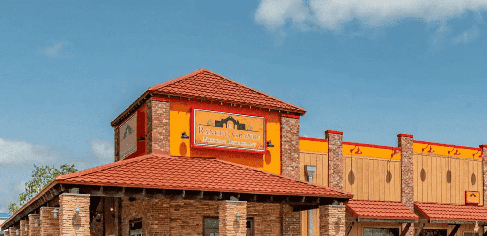 Brick restaurant exterior with red roof and sign, under a partly cloudy sky.